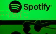 A screen displaying "Spotify" on a green backdrop with headphones laying in front of it.