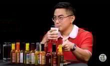 A man sits at a table covered in sauce bottles, sipping a glass of milk.