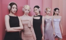 The members of Le Sserafim wearing Sony headphones and standing in front a pink wall.