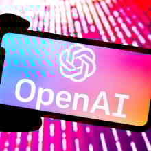 OpenAI logo open on a phone bathed in pink light.